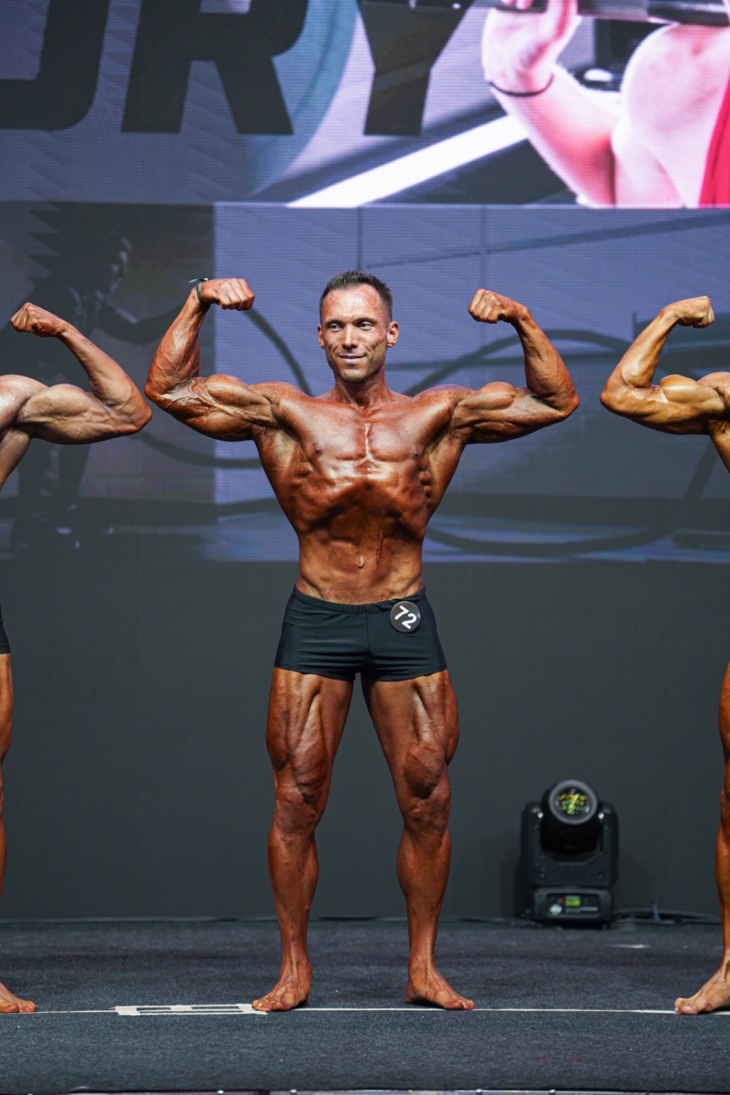 Süleyman Güngör Classic Physique sahnesinde ön çift biceps pozu verirken